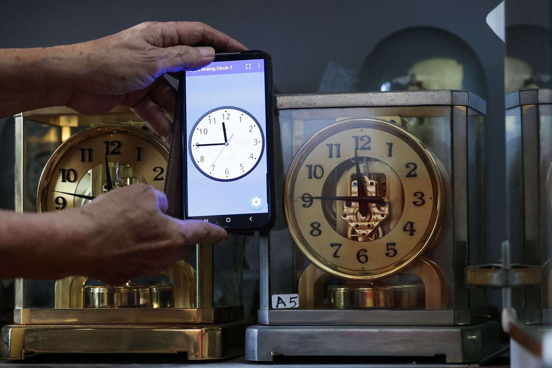 Mr Mun showing the accuracy of an ATMOS II (right) model, made in 1939, which very closely matches the time from a mobile phone.  No mechanical clock can be accurate all the time, without some deviations.