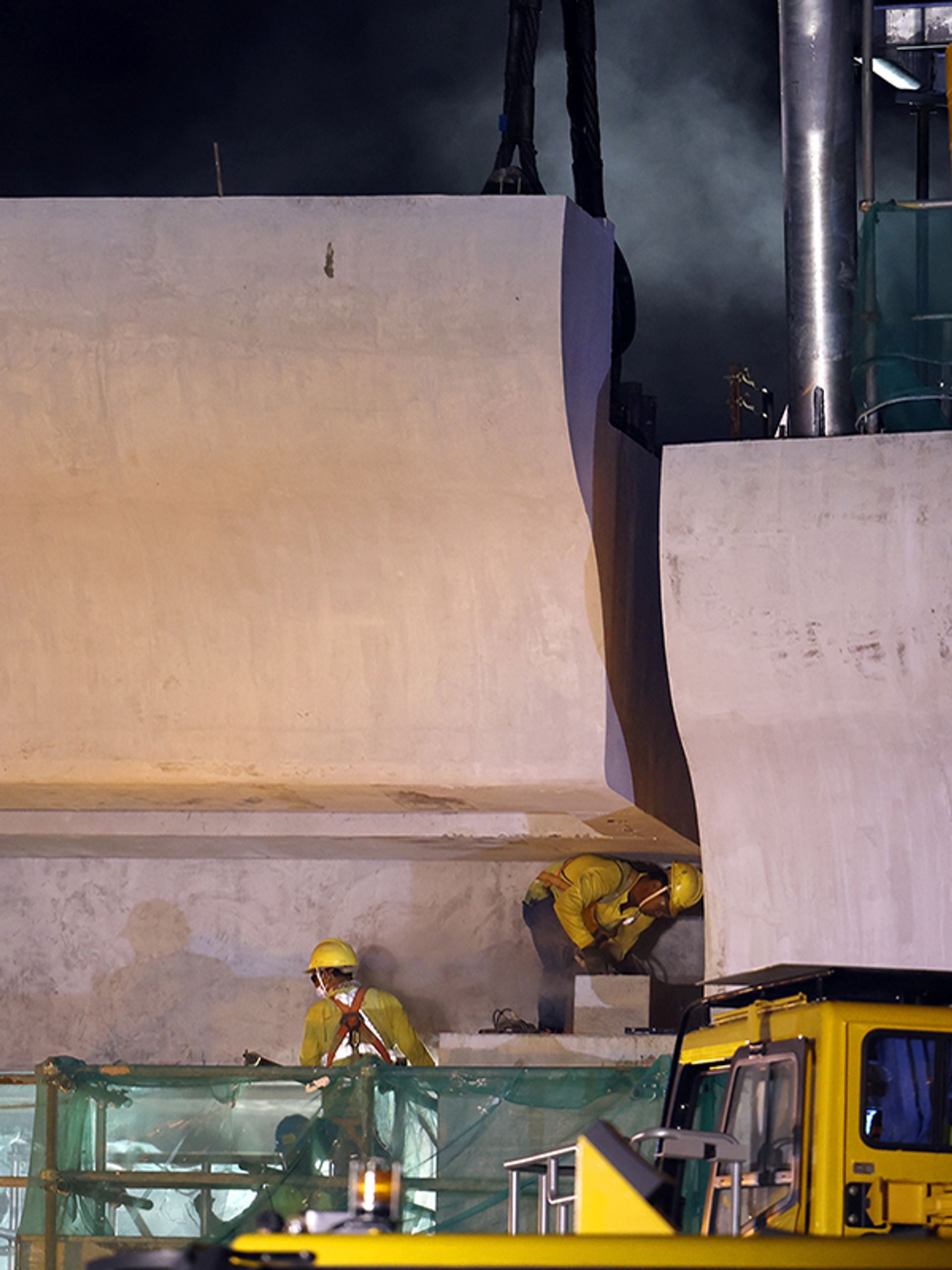A worker grinding the surface of the supporting column to ensure it fits with an already-installed segment of the bridge in the early hours of March 23